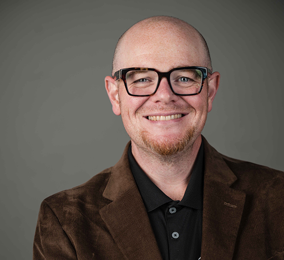A man in commencement regalia holds up his degree with Gonzaga University written on it